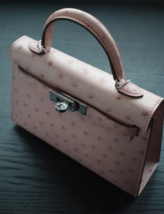 玫瑰鸵鸟凯莉手袋，结构化轮廓，银色五金，置于深色木质表面