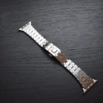 银色苹果手表表带，几何造型不锈钢链节，折叠式表扣，搭配深色木质表面