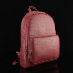 Wine red crocodile leather backpack with distinctive scale pattern and silver hardware on black background
