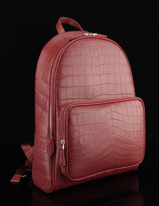 Wine red crocodile leather backpack with distinctive scale pattern and silver hardware on black background