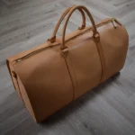 棕色植鞣革旅行包，配黄铜五金件和双提手，放置于木地板上